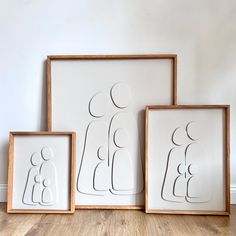 three framed artwork pieces sitting on top of a wooden floor