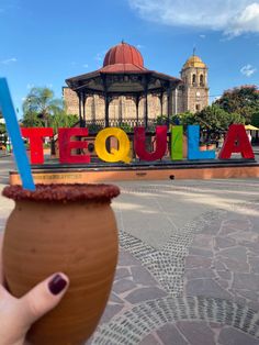 a hand holding up a chocolate drink in front of a sign that says tequila