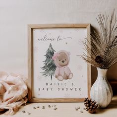 a baby shower sign with a teddy bear next to it and a pine cone on the table