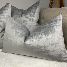 two gray pillows sitting on top of a couch next to a white furnishing