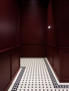 an empty room with red walls and black and white floor tiles on the floor is lit by a spot light