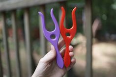 two plastic scissors are held up in front of a wooden fence with trees in the background