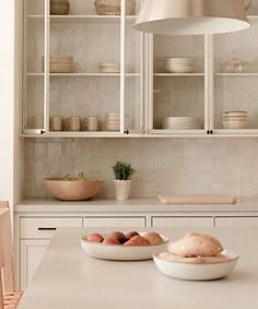 a kitchen with white cabinets and bowls on the counter top next to a light fixture