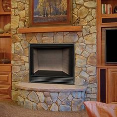 a stone fireplace in a living room with wooden shelves and paintings on the wall behind it