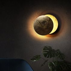 a wall mounted light with a moon on it and a plant in the corner next to it