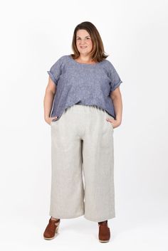 a woman standing in front of a white background wearing wide legged pants and a blue top