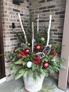 a potted plant with pine cones and ornaments on the front door sill for christmas