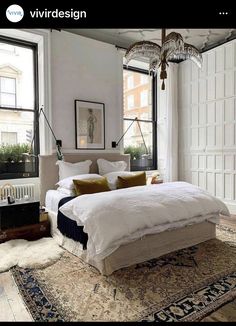 a bedroom with a large bed and lots of pillows on the floor next to two windows