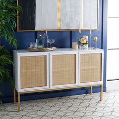 a white and gold sideboard with two mirrors on the wall next to a potted plant