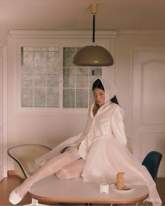 a woman sitting on top of a table in a white dress and veiled coat