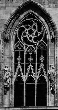 a black and white photo of an old church window with statues on the outside wall