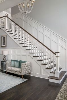 a living room filled with furniture and a chandelier hanging from the ceiling next to a stair case