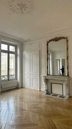 an empty room with wood flooring and large mirror on the wall above it's fireplace