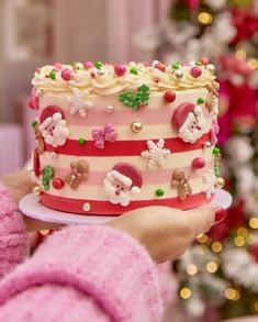 a person holding a cake decorated with christmas decorations and candy on it's side