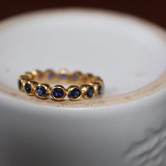 a gold ring with blue sapphires on it sitting on a white plate in front of a cup