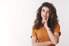 a woman with curly hair is posing for the camera and has her hand on her chin