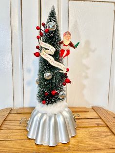 a small christmas tree on top of a tinsel skirted cake pan with decorations