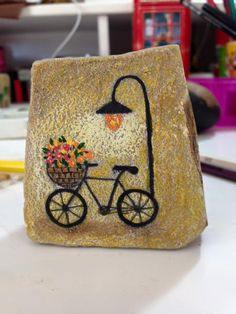 a rock with a bicycle painted on it and flowers in the basket next to it