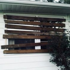 a window with wooden slats on the side of a white house next to a tree