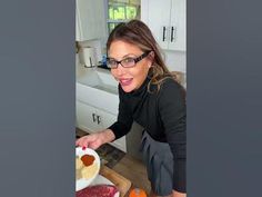 a woman in black shirt preparing food on top of a wooden cutting board with utensils