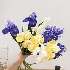 a hand holding a bouquet of blue and yellow flowers on top of a wooden table