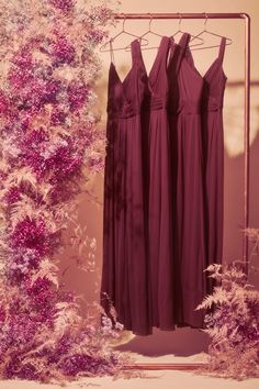 three bridesmaid dresses hanging on a rack in front of a flowery backdrop