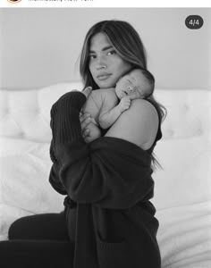 a black and white photo of a woman holding a baby in her arms while sitting on a bed