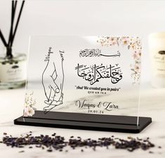 a glass plaque with an arabic calligraphy on it and some dried flowers in the background