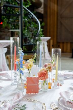 a table topped with lots of vases filled with flowers next to candles and plates