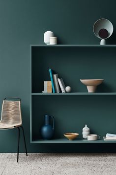 a green shelf with bowls and vases on it next to a chair in the corner