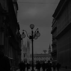 black and white photograph of people walking on street next to lamppost with cathedral in background