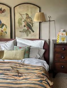 a bed with two paintings on the wall above it and a lamp next to it