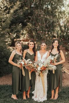 three bridesmaids in green dresses holding bouquets and smiling at the camera with trees in the background