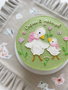 a cake decorated with two white ducks on top of a green plate and pink flowers