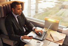 a man in a suit sitting at a table with a laptop and cell phone on his lap