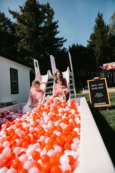 two girls in pink and white dresses are playing with orange and white balloons on the lawn