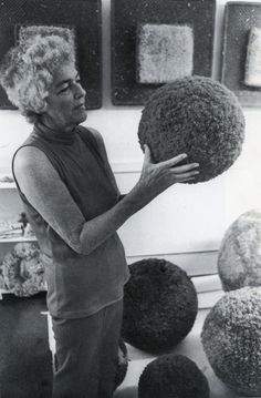 an older woman is holding a large piece of art in front of some balls on the floor