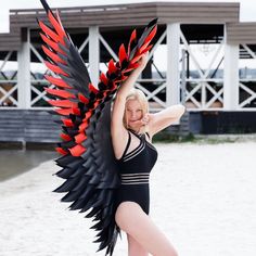 a woman in a black swimsuit with red and black wings on her back, posing for the camera