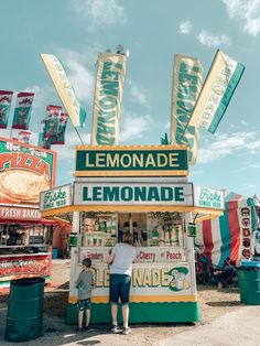 a man and child standing in front of a lemonade stand at an amusement park