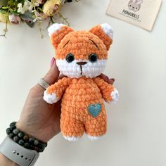 a hand holding a small crocheted teddy bear with a heart on its chest