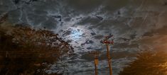 the sky is full of clouds and some power lines are in the foreground with trees on either side