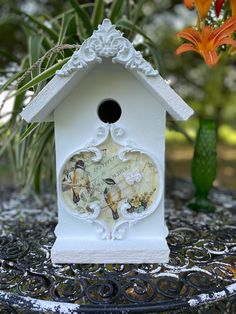 a white birdhouse sitting on top of a table next to a vase with flowers