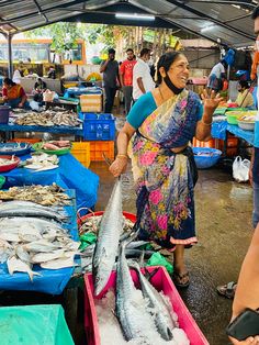 a woman standing in front of fish at an outdoor market