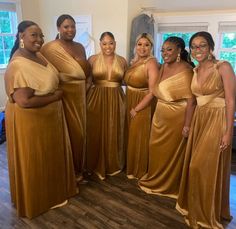 a group of women standing next to each other wearing gold dresses and posing for the camera