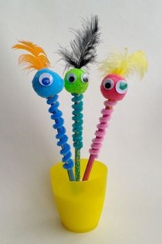 three different colored toothbrushes with googly eyes in a yellow cup on a white background