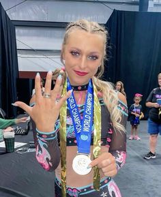 a woman holding up two medals in front of her face and hands, with other people behind her