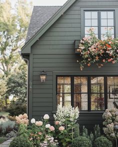 a gray house with flowers in the window boxes and plants growing on the front porch