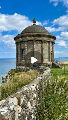 an old stone building sitting on top of a lush green hillside next to the ocean