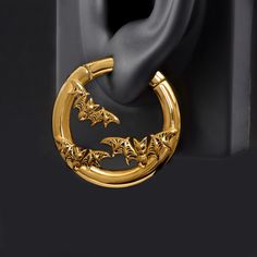 a pair of gold hoop earrings with bats hanging from it's side, on a black background