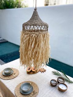 a table topped with plates and bowls next to a palm leaf covered chandelier